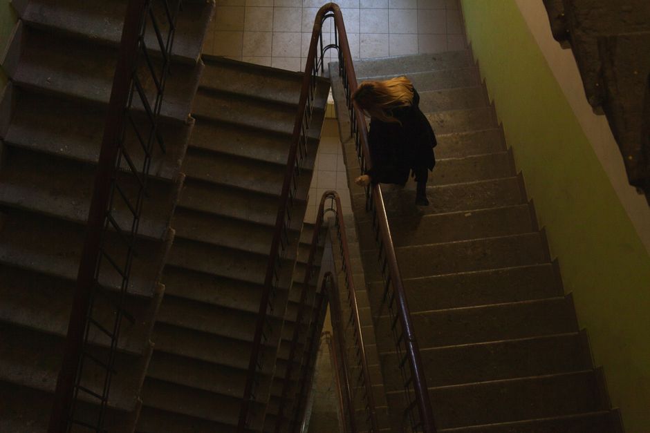 The exterior of a multi-storey residential building with an external staircase made of concrete and metal railings, leading to balconies on each floor. The building's facade features several windows and doors, with some balconies decorated with small plants and furniture. The staircase appears slightly weathered, with some paint chipping visible. A leafless tree is situated close to the building, partially obscuring the lower part of the structure. The scene is lit by natural daylight, suggesting daytime conditions. This image captures a typical urban residential environment, relevant to house removals and moving services, illustrating the logistical considerations of navigating staircases during a home relocation managed by Man with Van Ponders End.